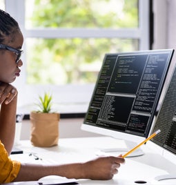 Woman sits coding at two monitors on her desk