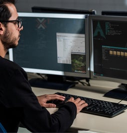 Man sits at desk with two monitors showing a Linux system