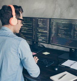 Rear view of a man working at two desktops coding