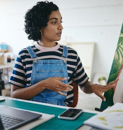 Creative woman gestures to her painting in front of her laptop