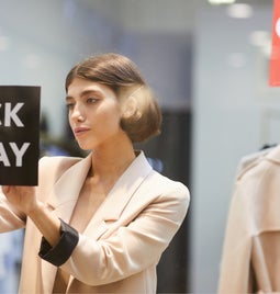 Shop owner places a Black Friday sign in the window, with sale sign visible in the background