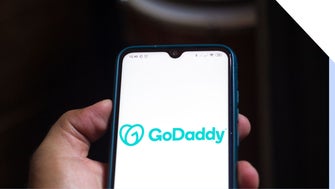A person holding a smartphone with a GoDaddy logo on the screen.