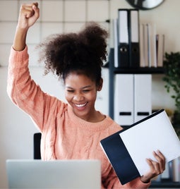 Lady punches air with joy in front of her laptop