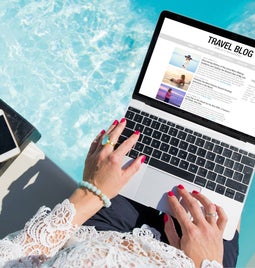 Woman sites on the edge of a pool using a laptop to work on a travel blog