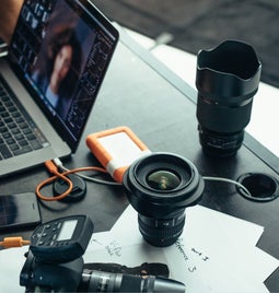 Desk covered in photography equipment and someone working on a laptop