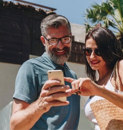 Vacationing couple smile at phone in the sun