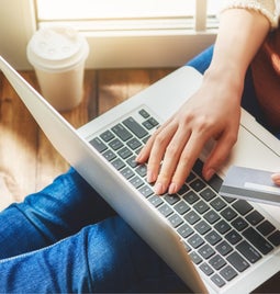 Laptop on lap with a hand holding a credit card