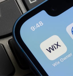 Phone on keyboard shows the Wix app and WordPress app side by side